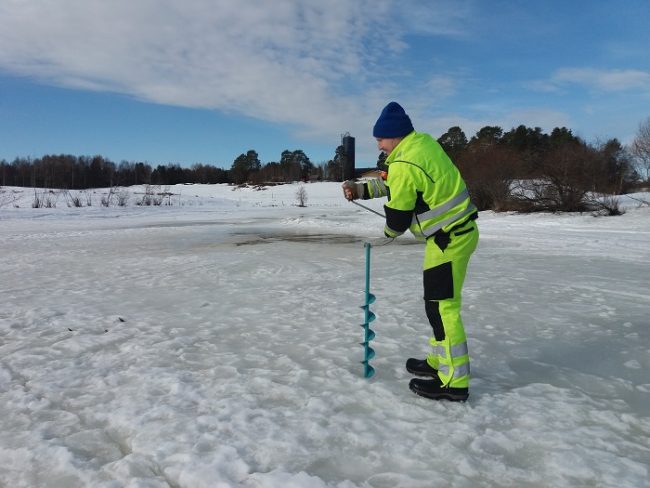 Pescador haciendo un agujero en el hielo con la barrena manual 