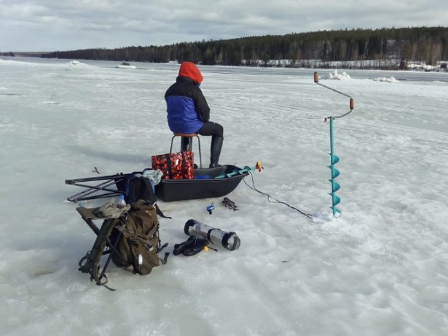 Pescando en un río helado. Se puede observar, entre otras cosas, la barrena de hielo y la mochila-silla 